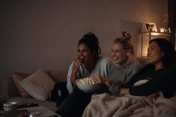 filmer om kvinnlig vänskap – tre kvinnor sitter i soffan och skrattar tillsammans med popcorn
