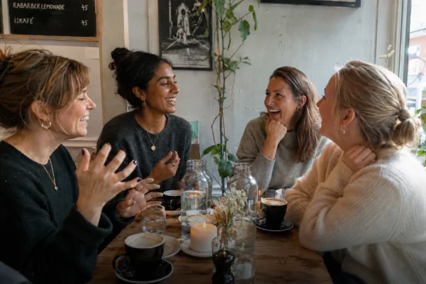 Hitta vänner med samma intressen – fyra kvinnor skrattar och fikar tillsammans på café