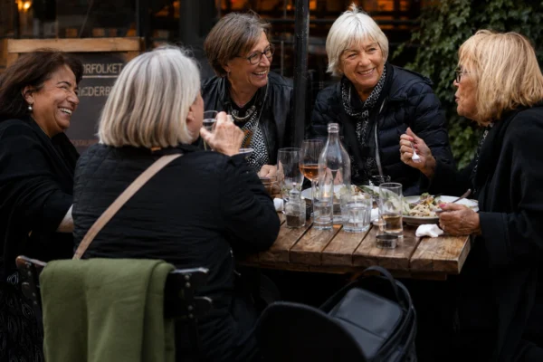 Hitta vänner som pensionär – fyra kvinnor skrattar och umgås över lunch utomhus