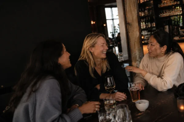 tips för att hitta nya vänner – tre kvinnor skrattar och umgås på en bar