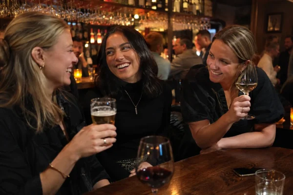 träffa vänner utan barn – tre kvinnor skrattar och umgås på en bar med öl och vin